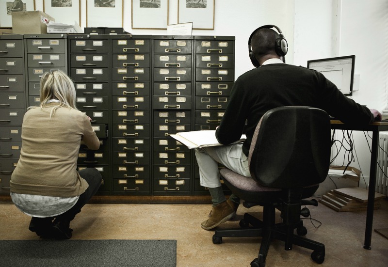 Aileen Campbell looking through the card catalogue with Drew Wright listening to recordings from the archive at a desktop computer.