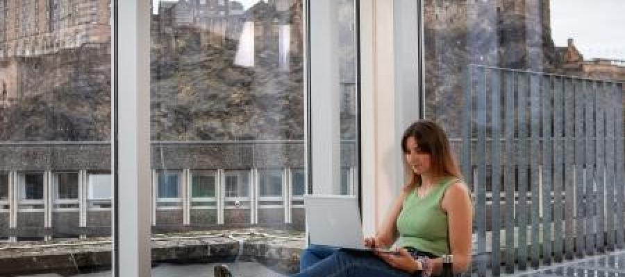 Student in front of window with backdrop of Edinburgh Castle