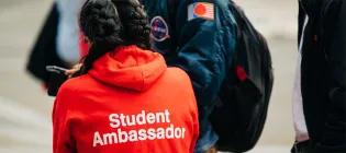 A student ambassador dressed in a red hoodie assists new students during welcome week.
