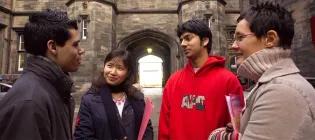 Four students engaged in conversation in front of New College, The University of Edinburgh.