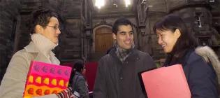 Three students engaged in conversation in front of New College, The University of Edinburgh.