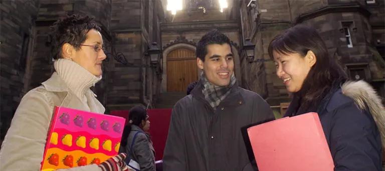 Three students engaged in conversation in front of New College, The University of Edinburgh.